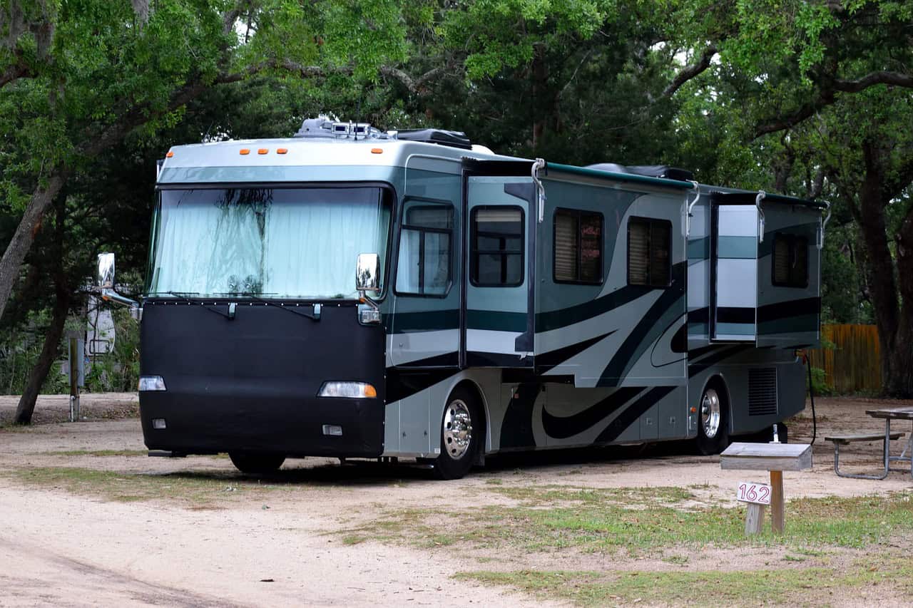 Wohnmobil parkt auf Campingplatz, Bäume im Hintergrund.