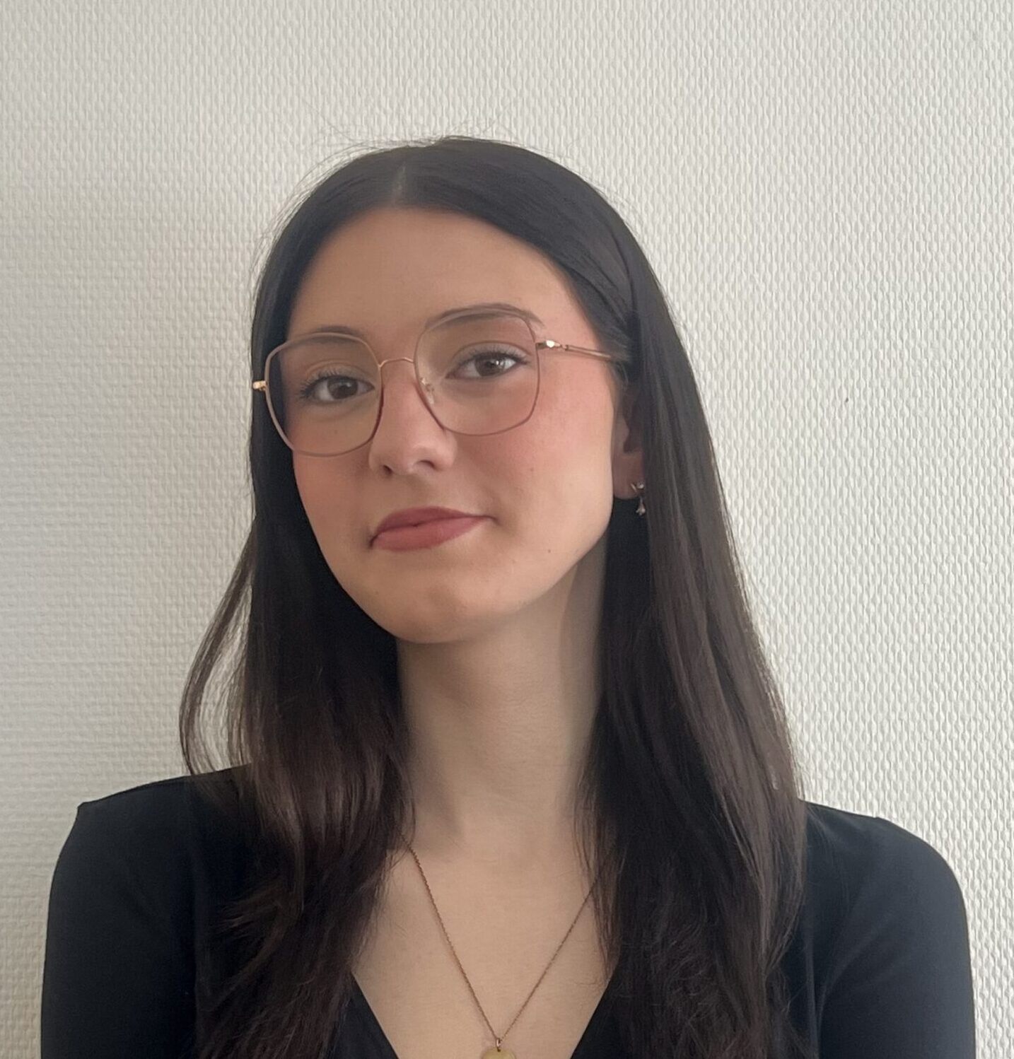 Person mit Brille und schwarzem Oberteil vor hellem Hintergrund.